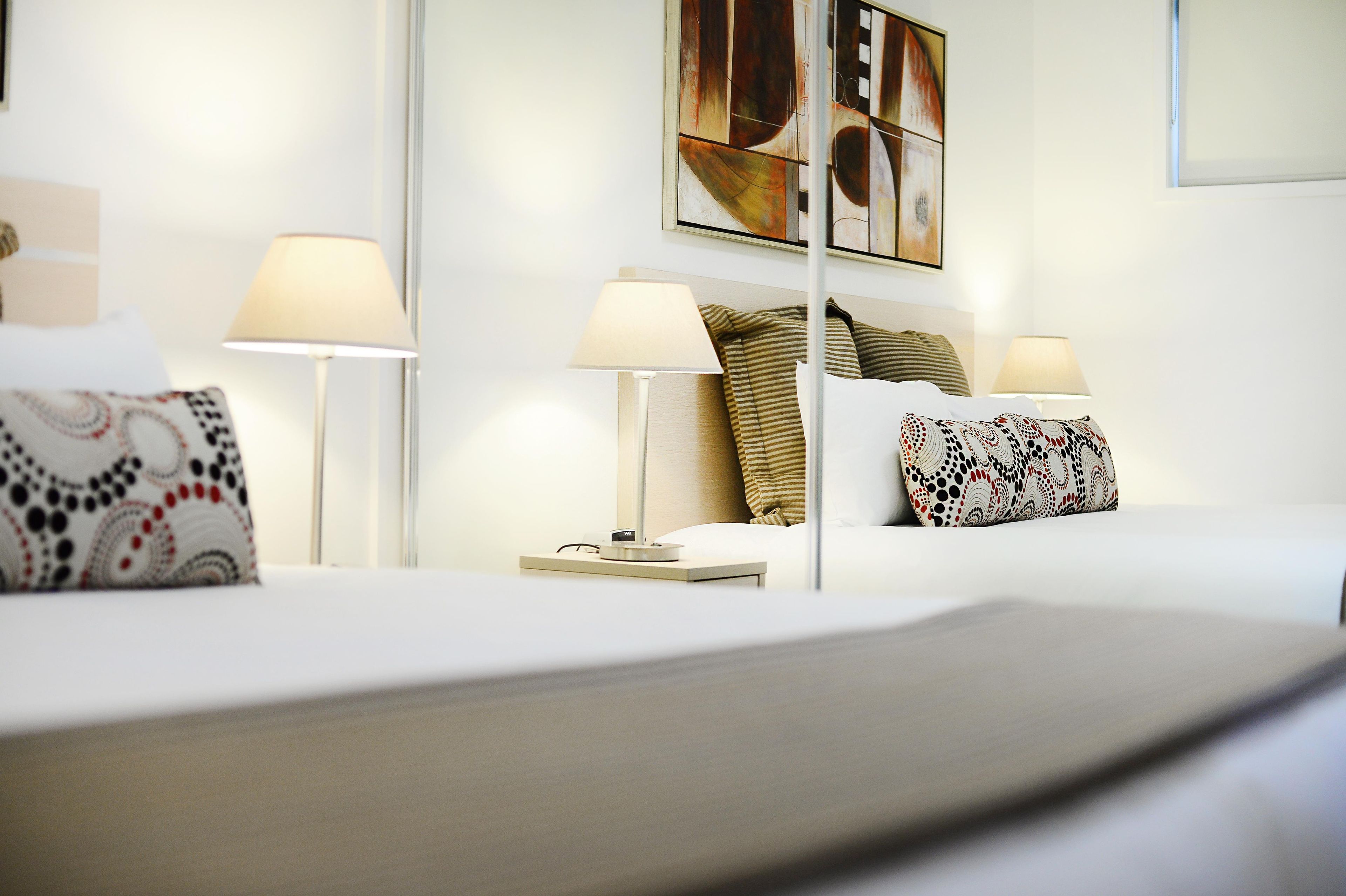 A hotel room with a bed, two bedside lamps, a nightstand, and a painting on the wall.