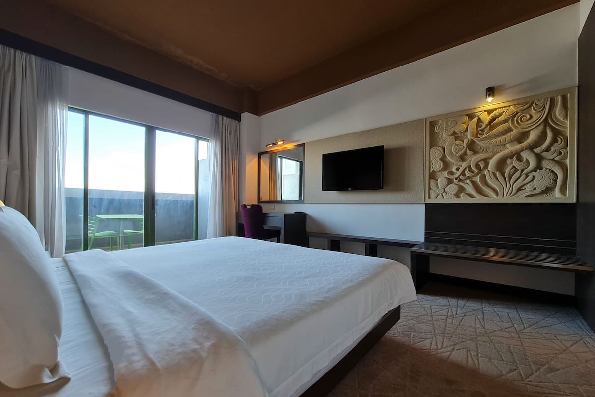 A hotel room with a large bed, a desk, a flat-screen TV, and a decorative wall panel.