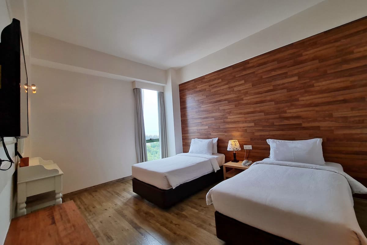 A hotel room with two beds, a wooden headboard, a small table with a lamp, and a TV.