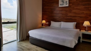 Un dormitorio con una cama grande, un panel de pared de madera, dos mesitas de noche con lámparas, una ventana con cortinas y un cuadro en la pared.
