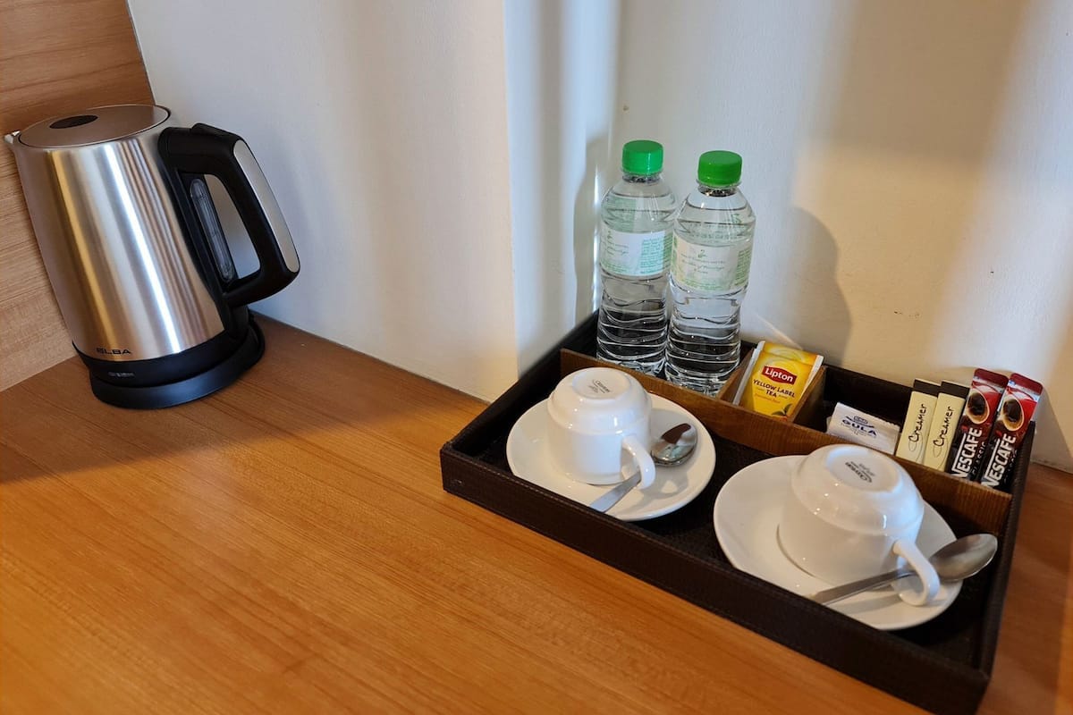 A tray with two cups, a spoon, two bottles of water, a box of Lipton tea, and a coffee maker on a wooden table.