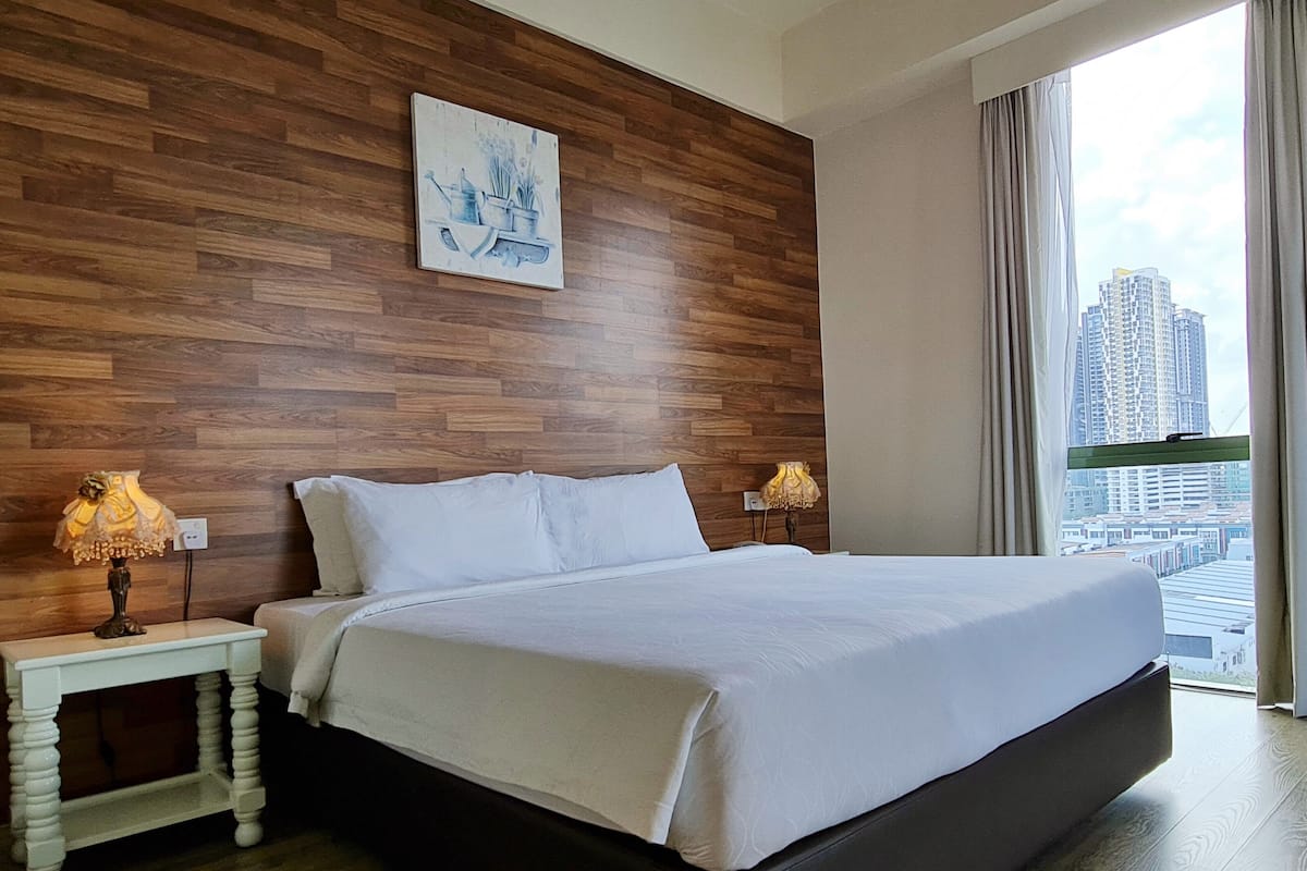 A modern hotel room with a large bed, wooden panel wall, and a city view.