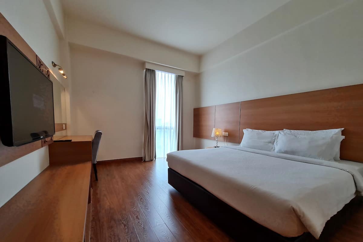 A hotel room with a large bed, a TV mounted on the wall, a desk, and a chair.