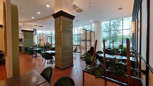 Un restaurante espacioso con techos altos, ventanas amplias y mobiliario moderno.