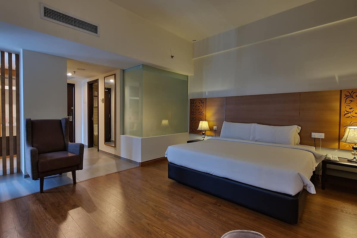 A hotel room with a large bed, a chair, a nightstand, and a wall with decorative paneling.
