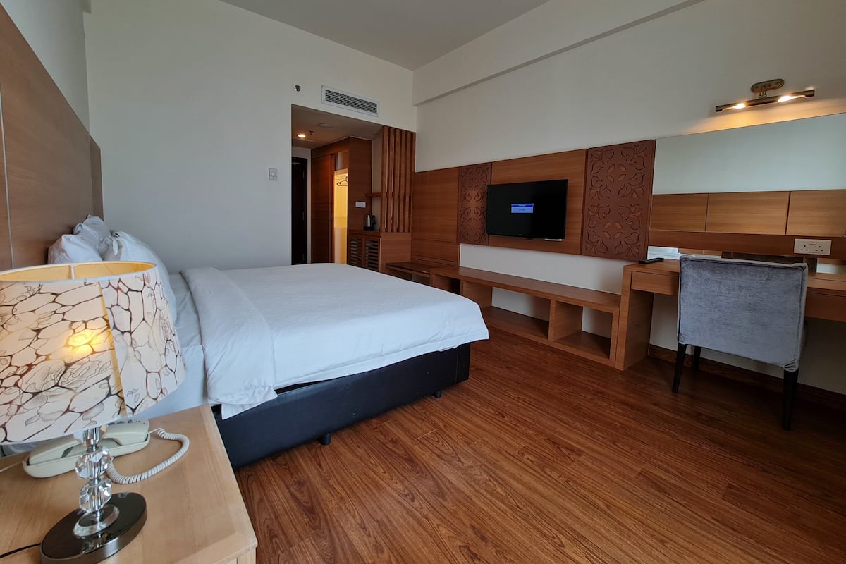 A hotel room with a bed, bedside table, lamp, desk, chair, TV, and wooden paneling.