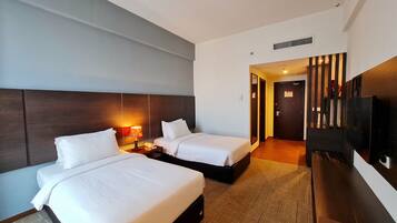 A hotel room with two beds, a TV, a desk with a lamp, and a door leading to another room.