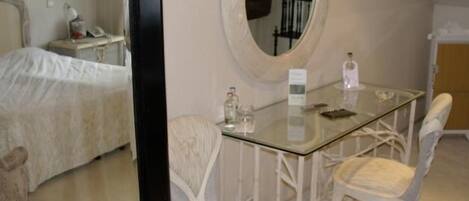 A hotel room with a bed, a glass table, a chair, a mirror, and a wardrobe.