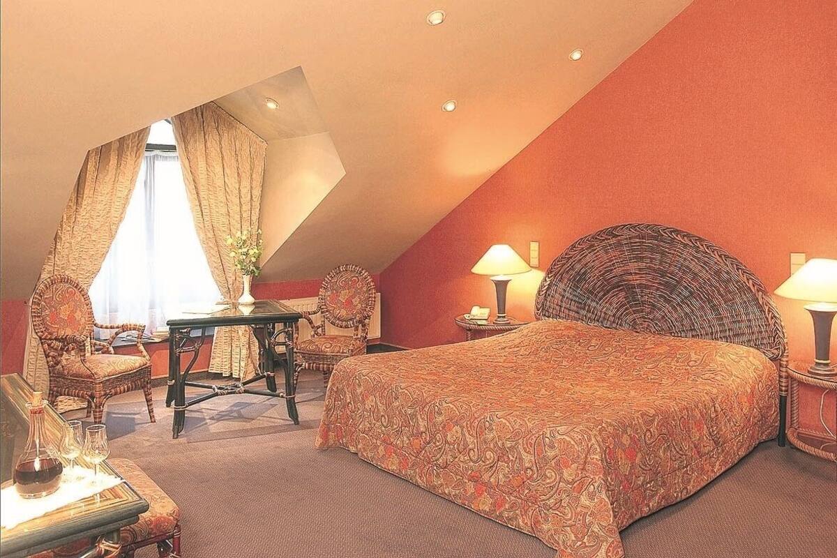 A bedroom with a large bed, two chairs, a small table, and a lamp.