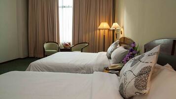 A hotel room with two beds, a desk, a chair, and a window with curtains.