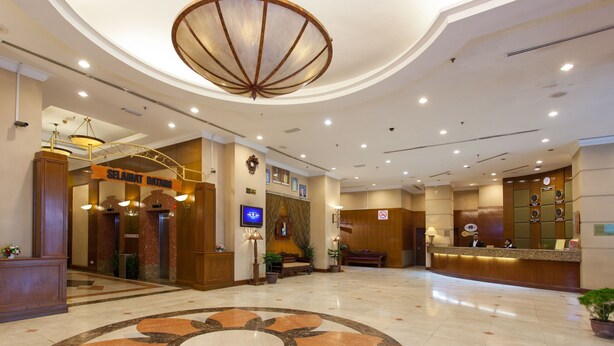 A spacious lobby with a large circular marble floor design, a reception desk, and a modern chandelier.