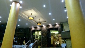 A hotel lobby with a staircase, a reception desk, and a chandelier.