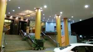 A hotel lobby with a staircase, columns, and a white car parked outside.