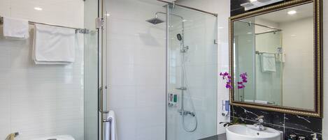 Un baño moderno con ducha envuelta en vidrio, inodoro blanco, suelo de mármol negro y un espejo grande con marco dorado.