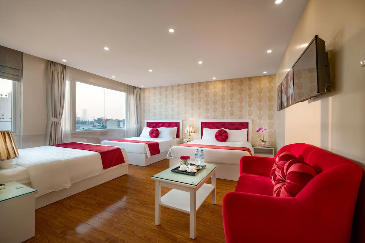 Habitació d'hotel amb dos llits, un sofà vermell, una taula petita amb una bandeja d'objectes i vista a la ciutat a través de finestres grans.