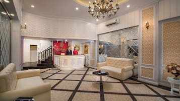 A hotel lobby with a reception desk, a staircase, a sofa, and a chandelier.