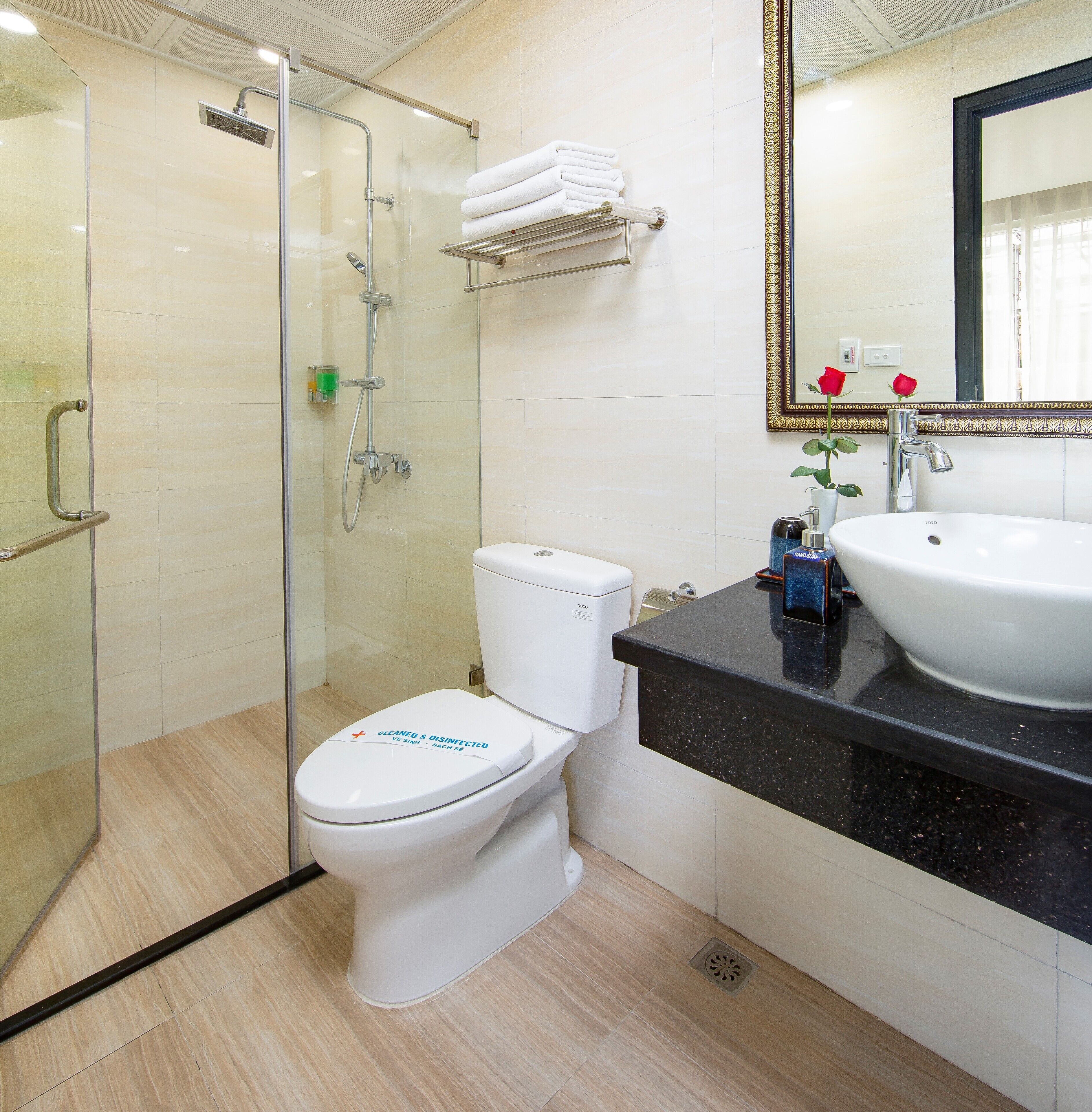 Een moderne badkamer met een glazen douchecabine, een wit toilet, een zwart aanrechtblad en een grote spiegel met decoratieve lijst.