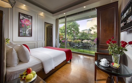 Habitación de hotel con cama, una mesa de comedor con un florero y vista al jard ín exterior.