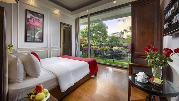 A hotel room with a bed, a dining table with a vase of flowers, and a view of the outside garden.