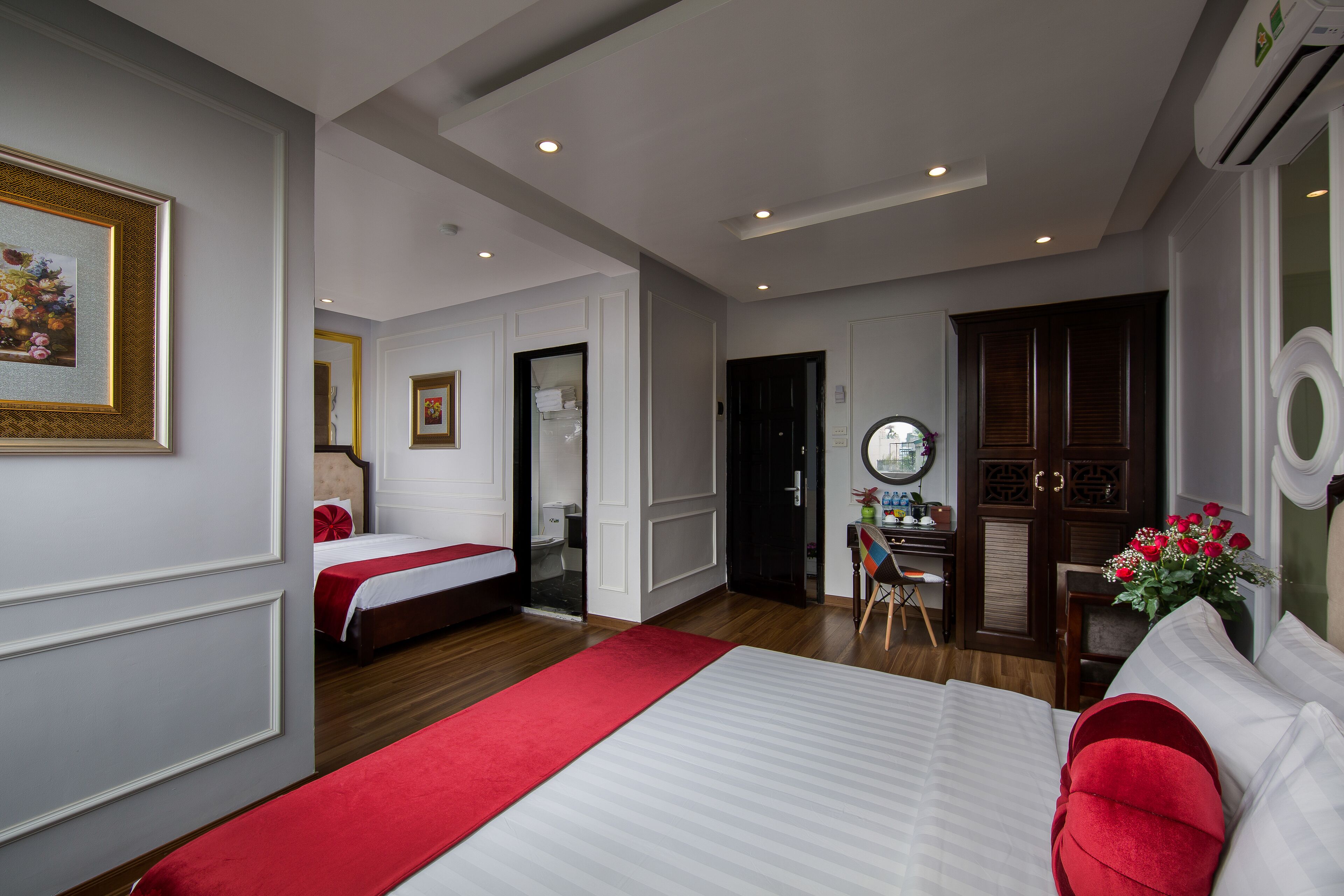 A hotel room with a large bed, a desk with a chair, a mirror, and a door leading to another room.