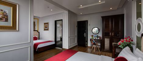 A hotel room with a large bed, a desk with a chair, a mirror, and a door leading to another room.