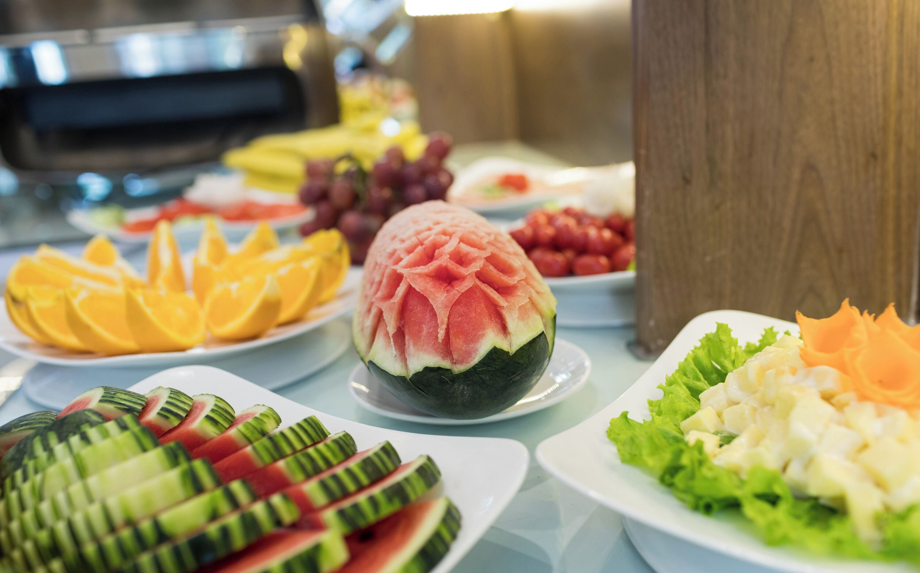 A buffet with various fruits and vegetables, including watermelon, oranges, and cucumbers.
