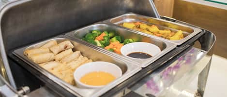 Un bufé con diversos alimentos, incluyendo rollitos primavera, brócoli, zanahorias y un recipiente con salsa.