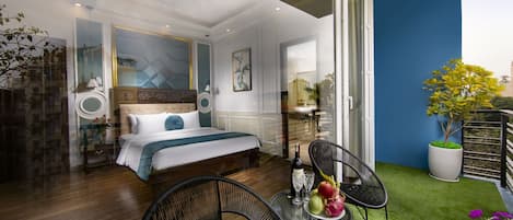 Un dormitorio moderno con una cama, dos sillas negras, una mesita con bebidas y un balcón con césped artificial y flores.