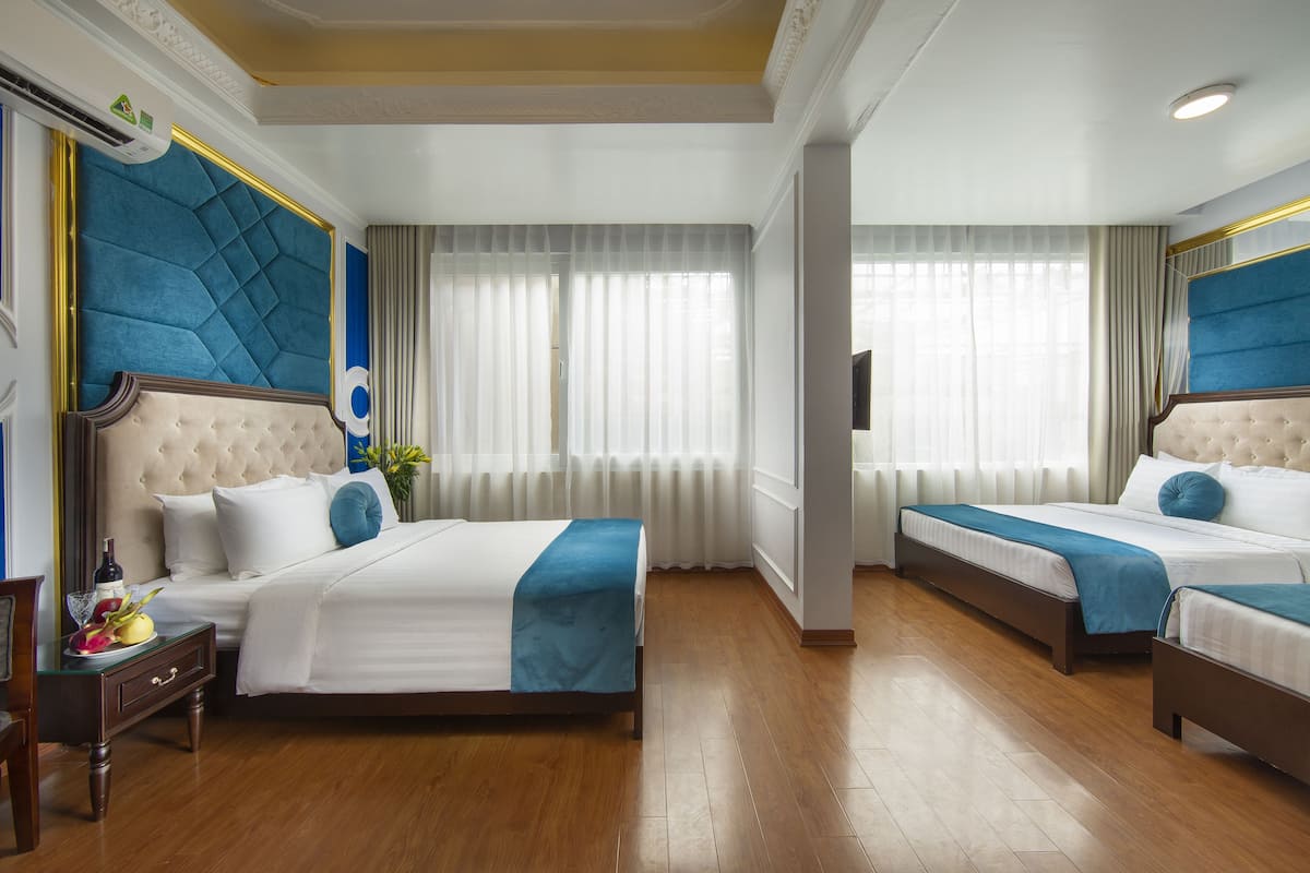 Habitació d'hotel amb dos llits, terra de fusta i una finestra gran amb cortines lleugeres.