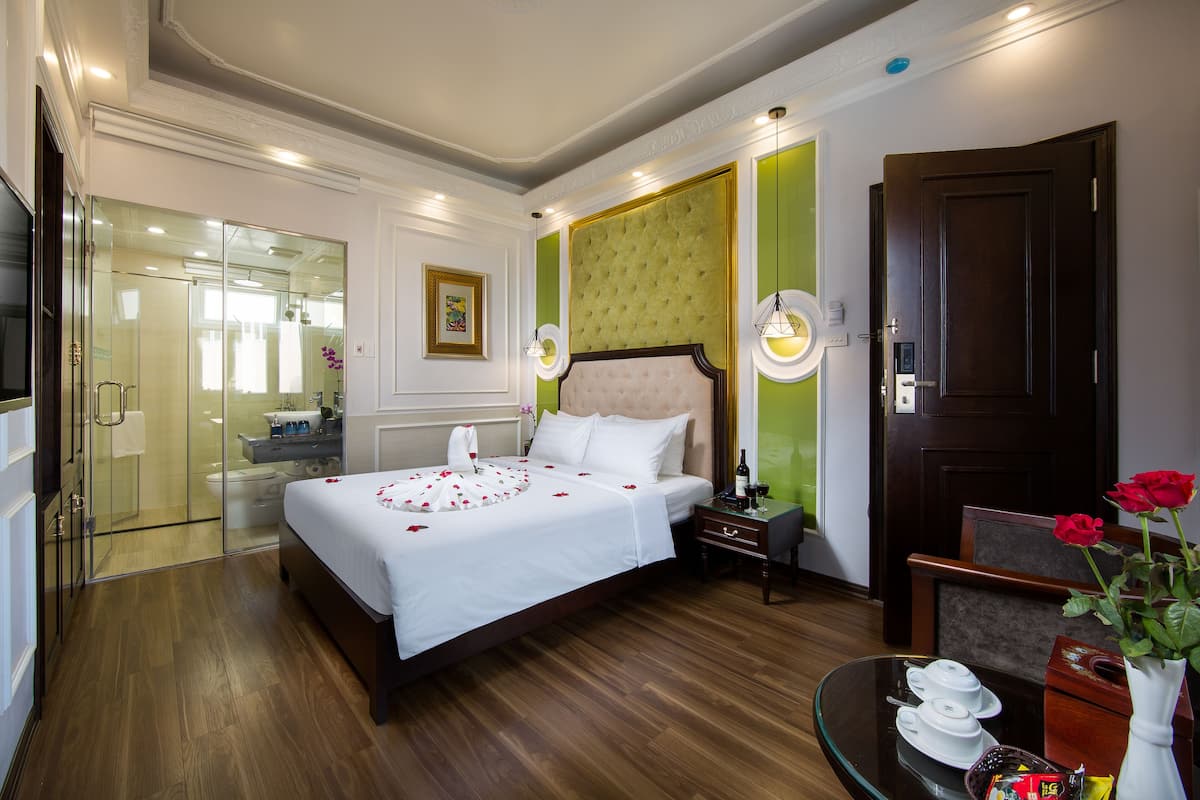 Habitació d'hotel amb un llit gran, un espai de banyera amb dutxa de vidre, terra de fusta i una paret d'accent verd.