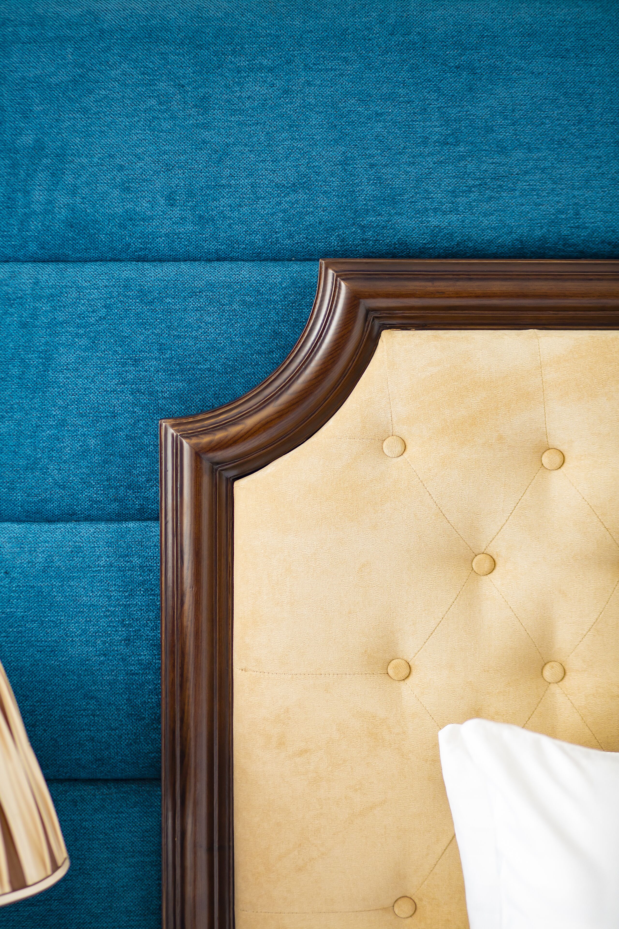 A tufted headboard with a wooden frame, set against a teal upholstered headboard.