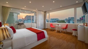 A modern hotel room with a large bed, a desk, two chairs, and a view of the cityscape.