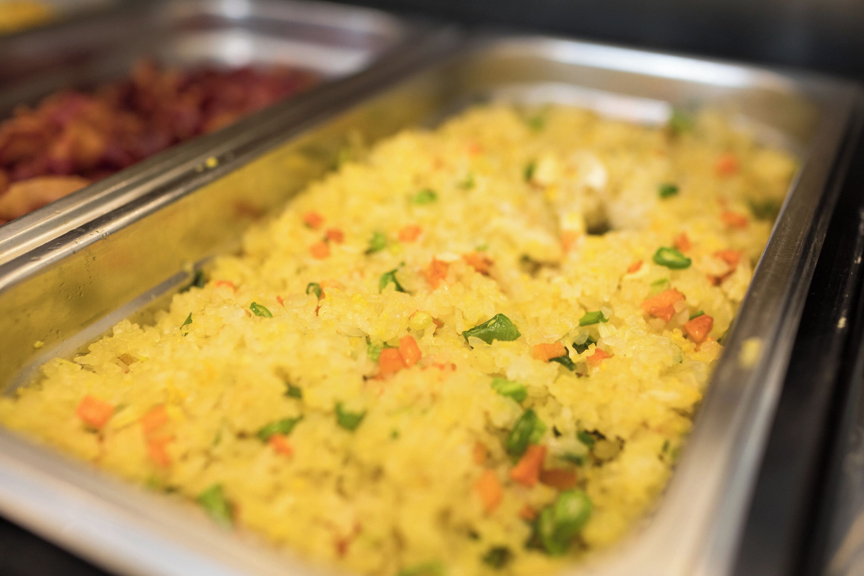A buffet with various dishes, including a section of yellow rice garnished with green herbs and diced vegetables.