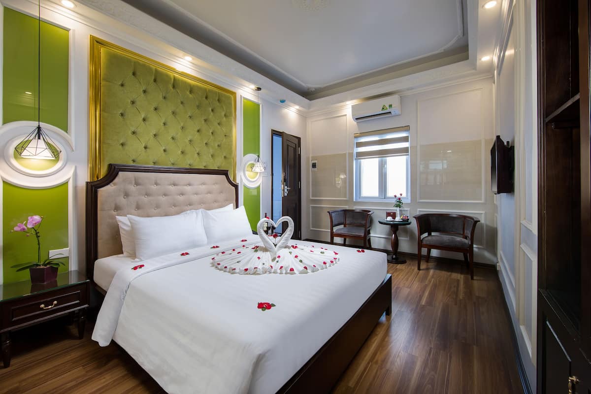 Una habitació d'hotel amb un llit gran, una paret d'accent verd, un capçal de llit amb textura, una taula petita amb cadires i una televisió.