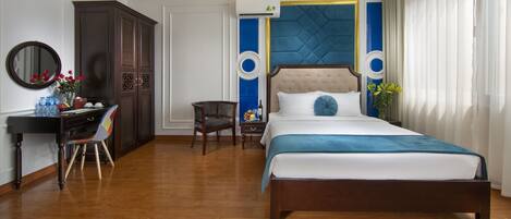 A bedroom with a large bed, a desk with a chair, a wardrobe, and a mirror.