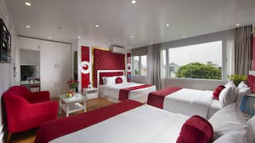 Habitación de hotel con dos camas, un sillón rojo, una mesita con un florero y vistas a la ciudad a través de amplios ventanales.