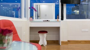 A modern kitchen with a white countertop, a red stool, and a large window with a TV mounted above it.