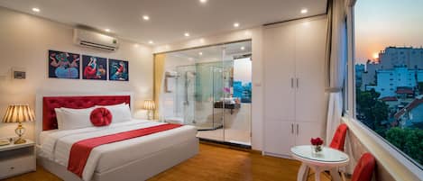 Habitación de hotel moderna con una cama grande, cabina de ducha de vidrio, una pequeña mesa con sillas y vistas a la ciudad a través de la ventana.