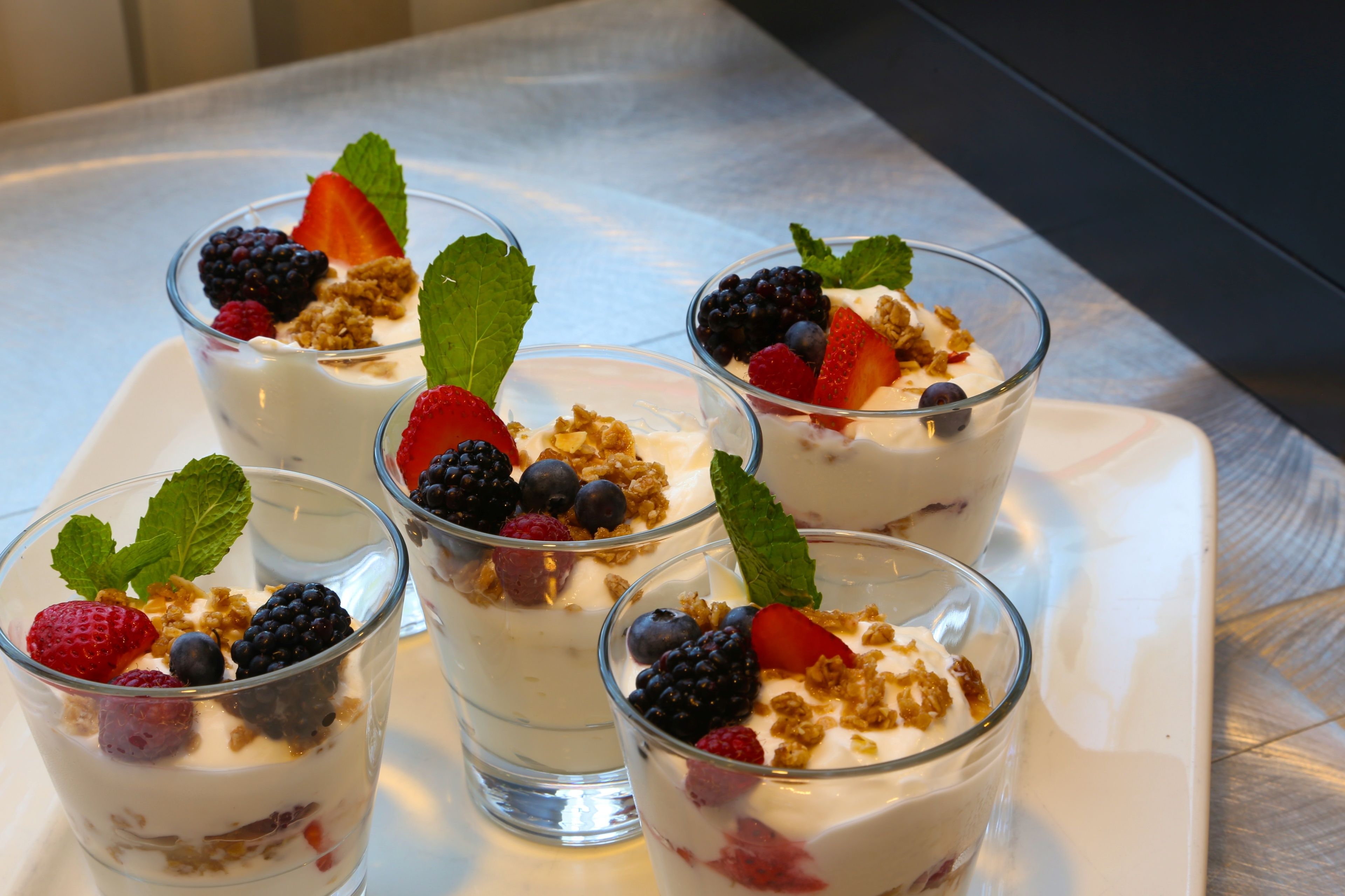Four glasses of yogurt parfait with berries and granola on a white plate.