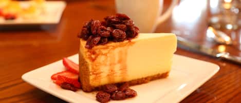 A slice of cheesecake with a fruit topping on a white plate, a white cup in the background, and a wooden table.