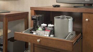 A hotel minibar with a coffee maker, a water dispenser, and a coffee pod dispenser.