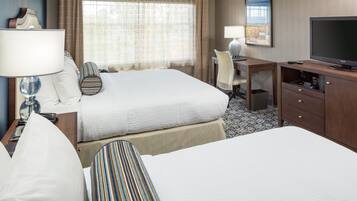 Ein Hotelzimmer mit zwei Betten, einem Schreibtisch, einem Fernseher und einem fenster mit Vorhängen.