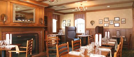 A dining area with wooden tables and chairs, a fireplace, and framed pictures on the walls.
