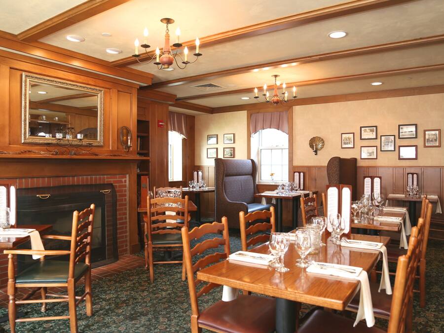 A dining area with wooden tables and chairs, a fireplace, and framed pictures on the walls.