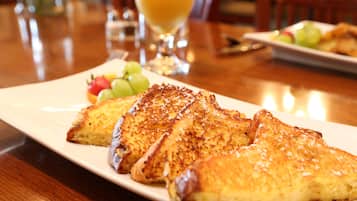 A plate of toasted bread with a side of fruit and a glass of orange juice on a wooden table.