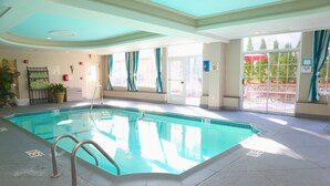 Una piscina interior con agua cristalina, una escalera metálica y suelo de baldosas.