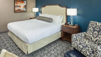 A hotel room with a large bed, two bedside tables with lamps, a patterned armchair, and a small table with a telephone.