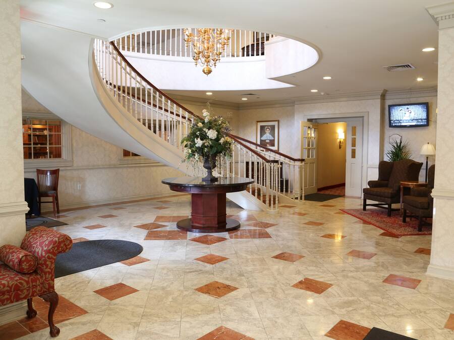 A spacious lobby with a grand staircase, a central floral arrangement, and a seating area.