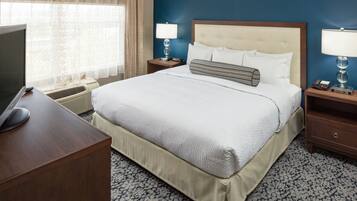 A hotel room with a large bed, two bedside tables with lamps, a desk with a computer and mouse, and a window with curtains.