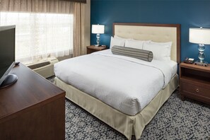 A hotel room with a large bed, two bedside tables with lamps, a desk with a computer and mouse, and a window with curtains.